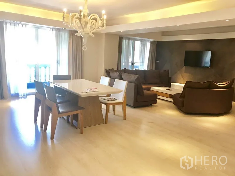 Condominium for rent in Watthana, Bangkok - Spacious living and dining room with chandelier, balcony doors and a brown sectional sofa.
