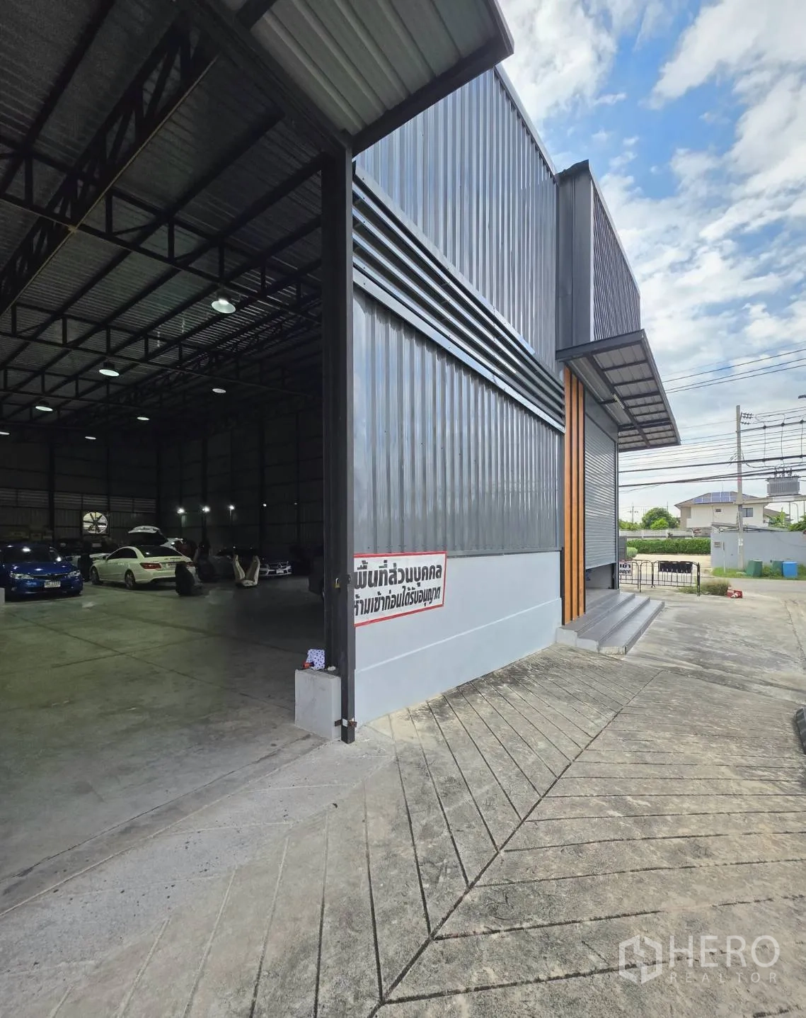 Warehouse for rent in Khlong Toei, Bangkok - Side view of the warehouse showing an open roller door, high-ceiling interior and sloped driveway for truck access.
