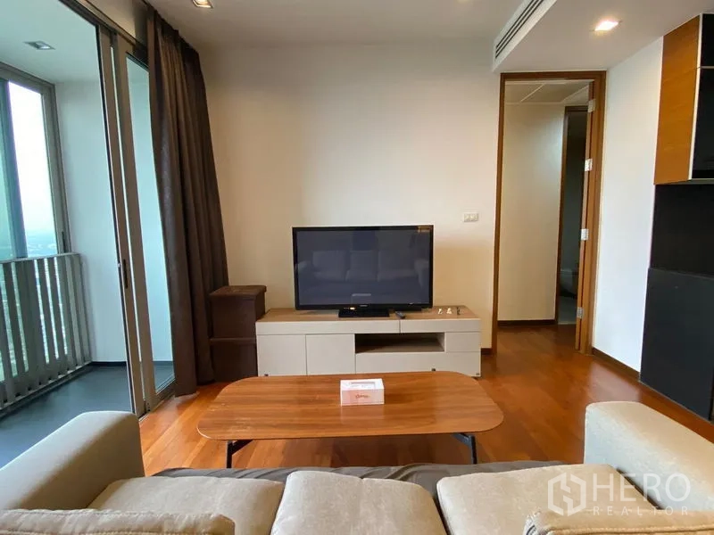 Condominium for rent - Cozy lounge with TV unit and coffee table, sliding doors to a covered balcony and hallway to bedrooms.