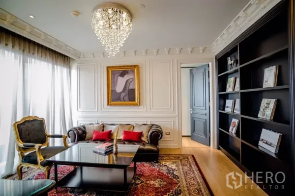Condominium for rent in Khlong Toei, Bangkok - Elegant living room in Bangkok condo with crystal chandelier, leather sofa, ornate wall moulding and full-height windows beside a black built-in bookcase.