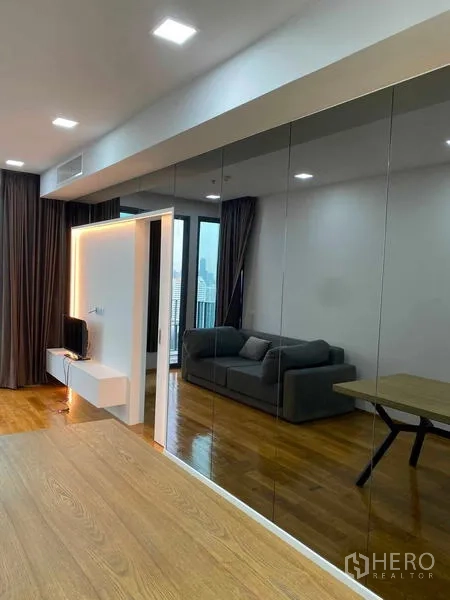 Condominium for rent or sale in Khlong Toei, Bangkok - Open-plan lounge featuring floor-to-ceiling mirrored wardrobes, sofa and access to the balcony.