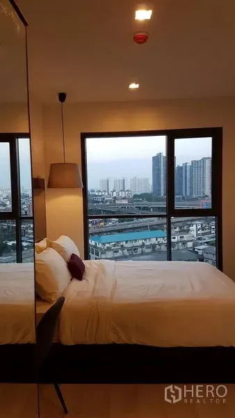 Condominium for rent in Khlong Toei, Bangkok - Corner bedroom with wide windows showcasing Bangkok skyline and warm lighting.