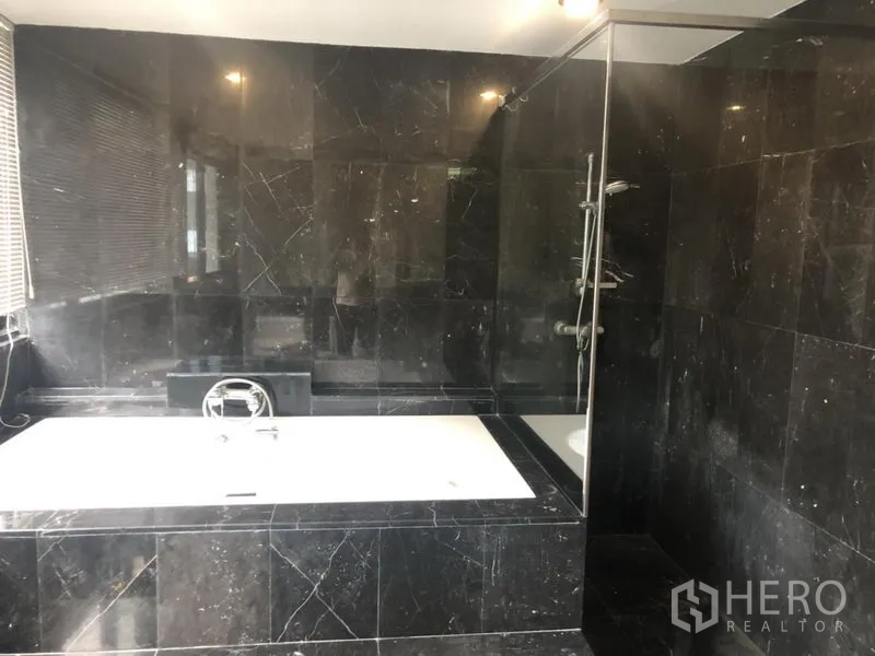 Condominium for sale in Watthana, Bangkok - Bathroom finished in black marble with a bathtub and glass-enclosed shower.
