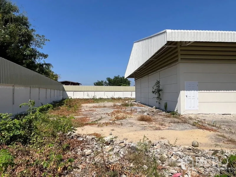 Warehouse for rent or sale - Rear corner yard with high fence and a metal-roofed warehouse building.