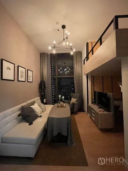 Condominium for rent in Ratchathewi, Bangkok - Double-height living room with chandelier, sofa and mezzanine TV corner.