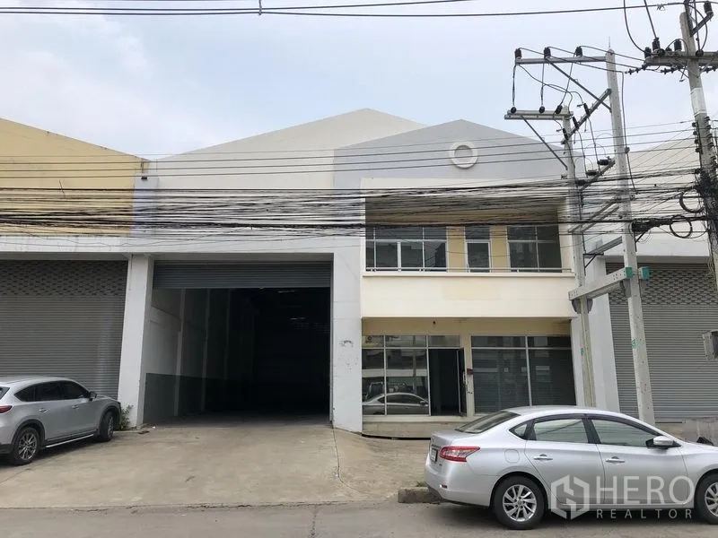 工厂 出租在Pathum Thani - 巴吞他尼Khlong Luang工厂外观，宽大卷闸门、两层办公室与前方停车区。