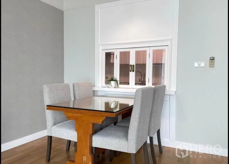 Condominium for rent in Sathon, Bangkok - Dining area with glass-top table and four upholstered chairs by a serving window.