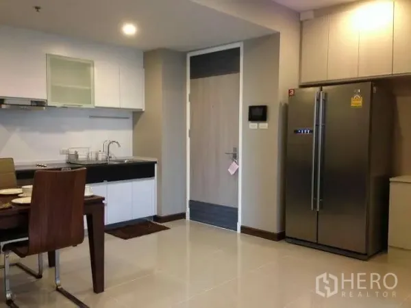Condominium for rent or sale in Huai Khwang, Bangkok - Kitchen corner featuring stainless double-door refrigerator, sink, dining set and the main entrance door.