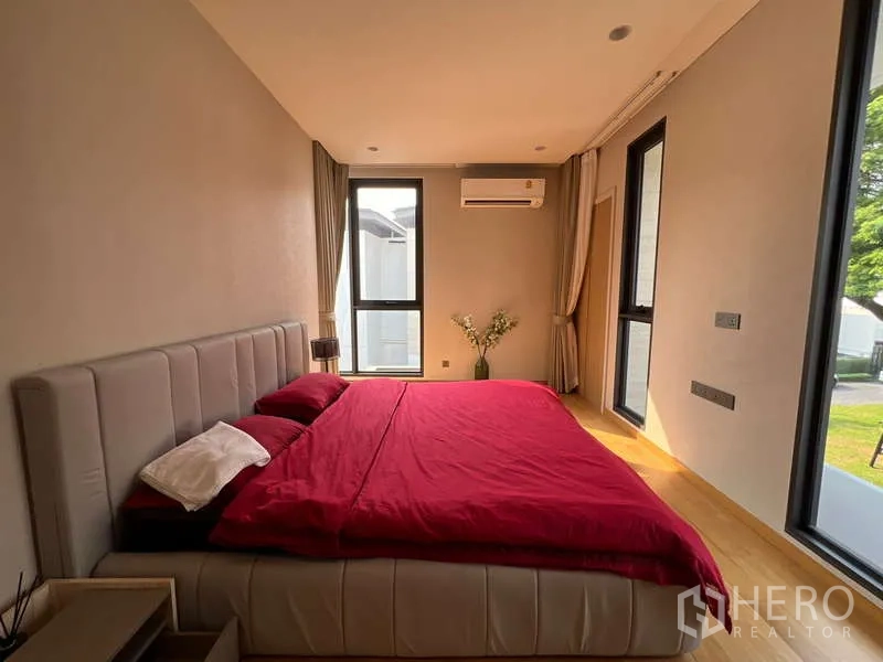 Detached House for rent in Suan Luang, Bangkok - Secondary bedroom with red bedding, corner windows and air conditioning.