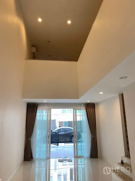联排别墅 出租在Bang Na, Bangkok - 开放式客厅，嵌灯照明，推拉门通向前庭与车位