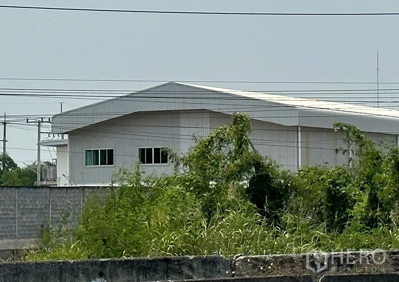 Factory for sale in Lat Lum Kaeo, Pathum Thani - Modern white factory with gable roof and windows behind a perimeter wall and greenery in Lat Lum Kaeo.