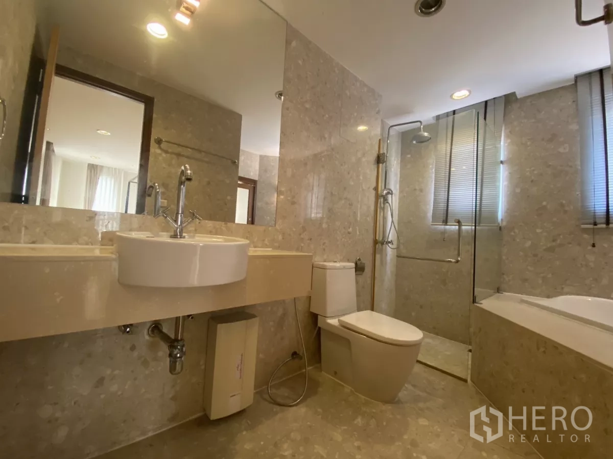 Condominium for rent in Watthana, Bangkok - Master bathroom with long vanity, toilet, glass shower and soaking tub in stone tile.