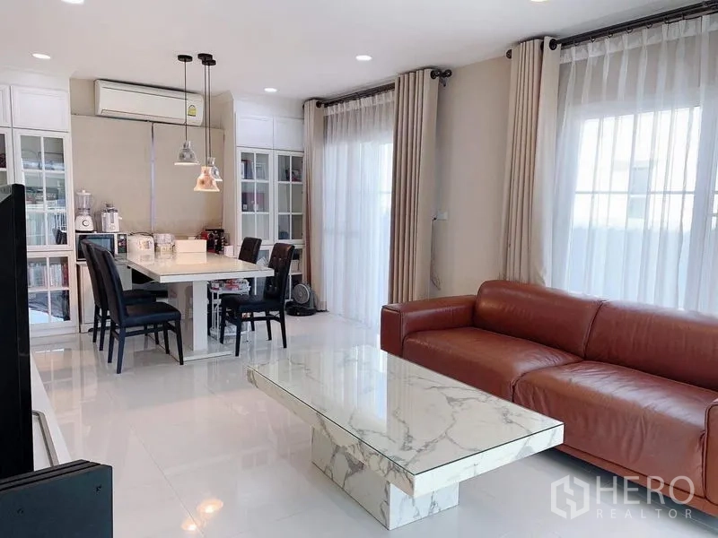 บ้าน ให้เช่าหรือขายในBang Phli, Samut Prakan - ห้องนั่งเล่นและรับประทานอาหารโปร่งสว่าง โซฟาหนังสีน้ำตาล โต๊ะหินอ่อน และม่านโปร่ง