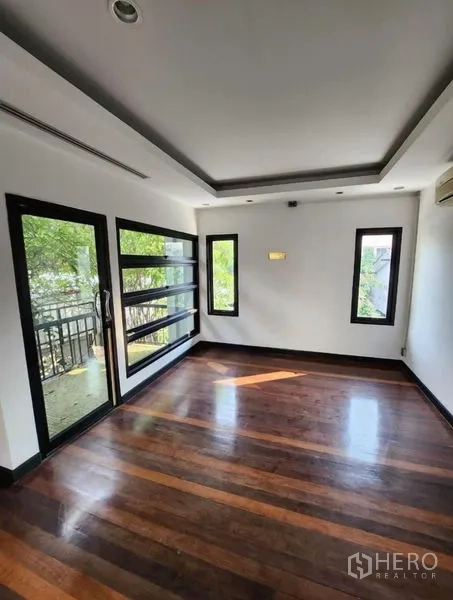Home Office for rent in Lat Phrao, Bangkok - Sunlit office or bedroom with balcony door, horizontal strip windows and hardwood flooring.