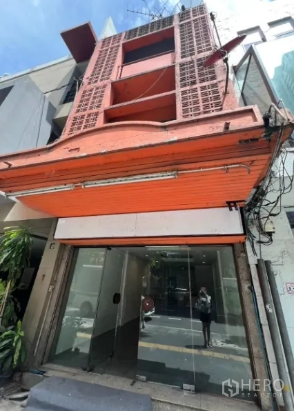 店屋 出租在Khlong Toei, Bangkok - 临街三层商铺外立面，橙色卷帘门与玻璃门头。
