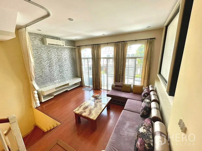 Townhouse for rent in Saphan Sung, Bangkok - Living room view to the front with full‑height windows, curtains and a textured feature wall.