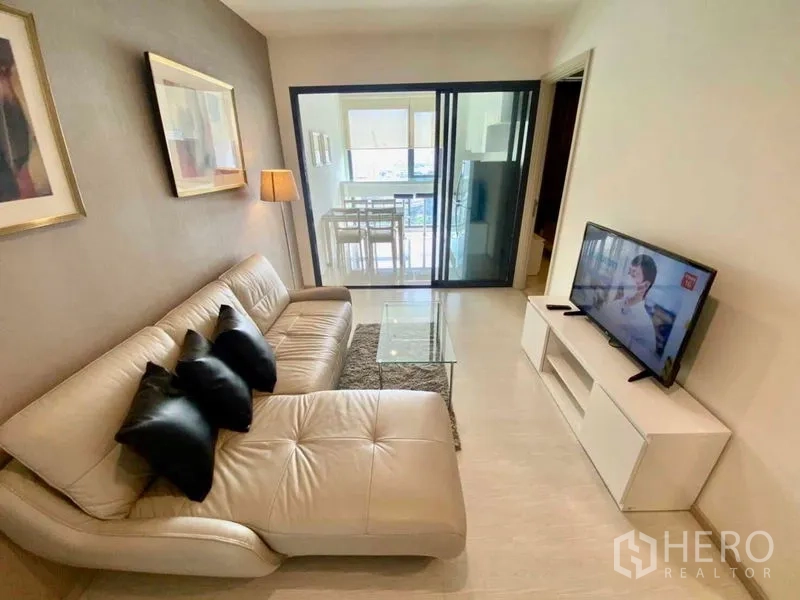 Condominium for rent in Khlong Toei, Bangkok - Living area facing the TV and sofa with a glass partition to the kitchen in neutral decor.