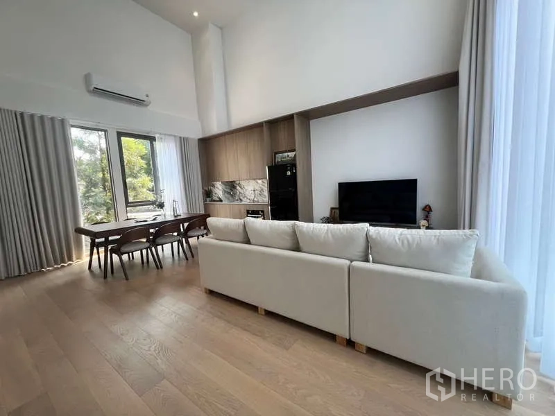 Townhouse for rent in Phra Khanong, Bangkok - Spacious living and dining room with high ceilings, wall kitchen and sheer curtains.