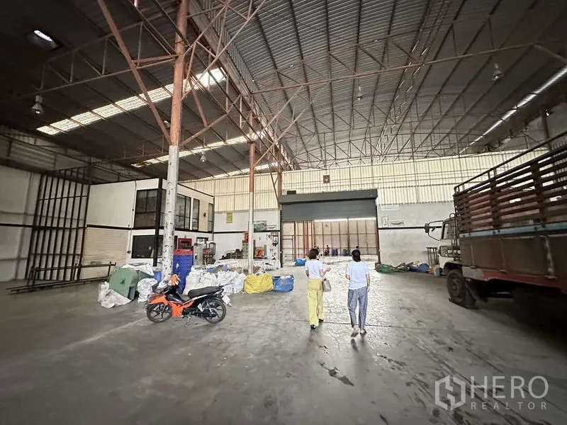 Factory for rent in Bang Bua Thong, Nonthaburi - Open-span warehouse with steel columns, materials on the floor and a roller door.