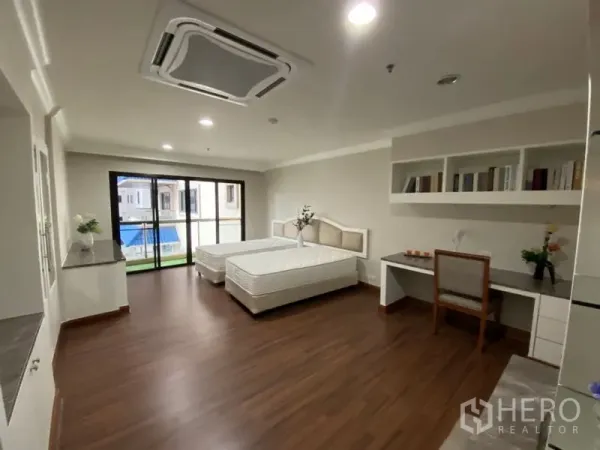 Condominium for rent in Watthana, Bangkok - Large twin bedroom with study desk, wall shelving, and sliding glass doors to the balcony.