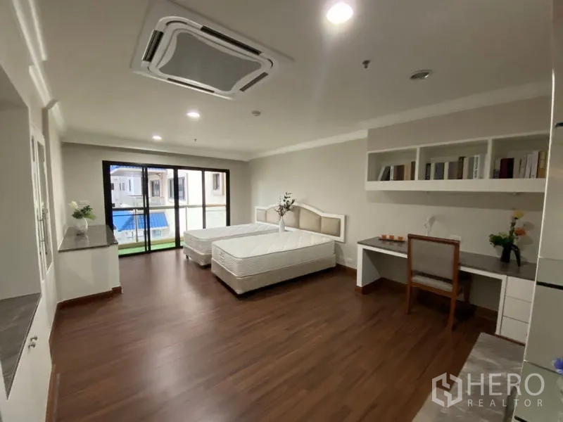 Condominium for rent in Watthana, Bangkok - Large twin bedroom with study desk, wall shelving, and sliding glass doors to the balcony.