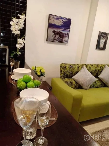 Condominium for rent in Khlong Luang, Pathum Thani - Breakfast bar set with glassware beside a green sofa in the open-plan living area.