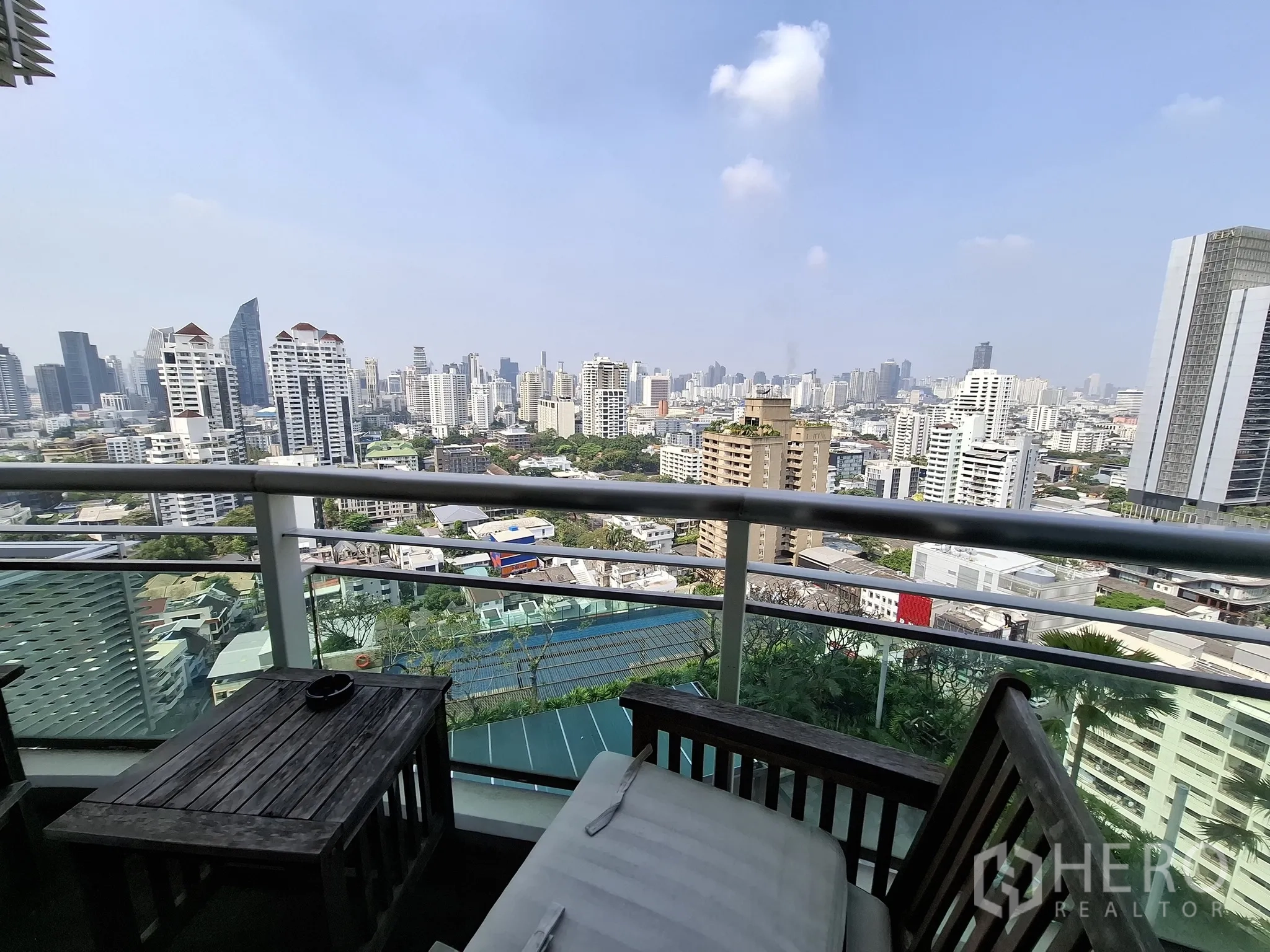 Condominium for rent in Watthana, Bangkok - High-floor balcony with glass railing and outdoor chairs facing Bangkok skyline.