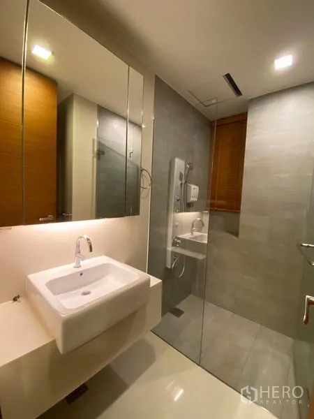 Condominium for rent in Khlong Toei, Bangkok - Modern bathroom with glass walk-in shower, vanity and mirrored cabinets.