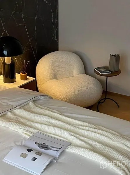 Condominium for rent or sale in Khlong Toei, Bangkok - Bouclé lounge chair and side table next to the bed against a dark marble feature wall.