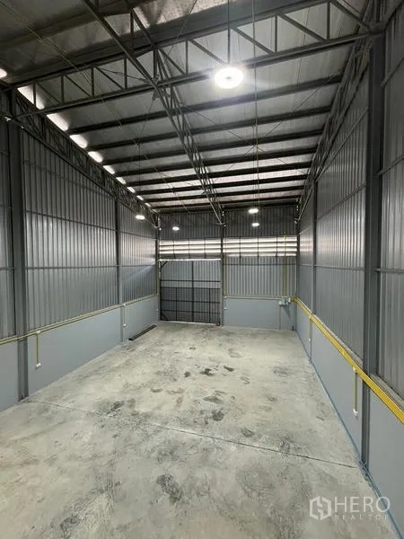 Warehouse for rent in Mueang Pathum Thani, Pathum Thani - Overhead look at the steel truss roof, bright lights and the main loading door.