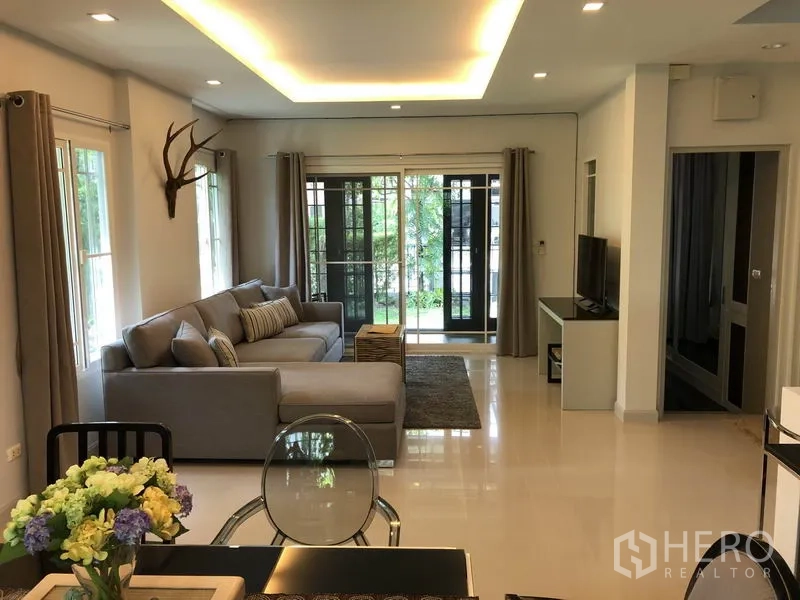 Detached House for rent or sale in Bang Kapi, Bangkok - Bright living room with L-shaped sofa, TV console, recessed ceiling lights and sliding doors to the garden.