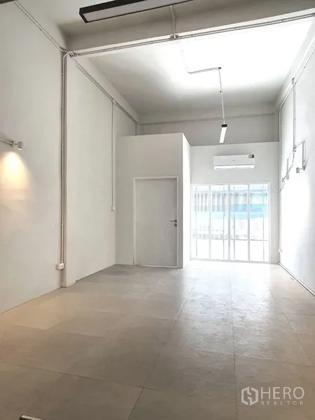 Shophouse for rent in Phra Khanong, Bangkok - Bright double-height front room with glass sliding door and wall-mounted air conditioner in a Bang Chak shophouse.