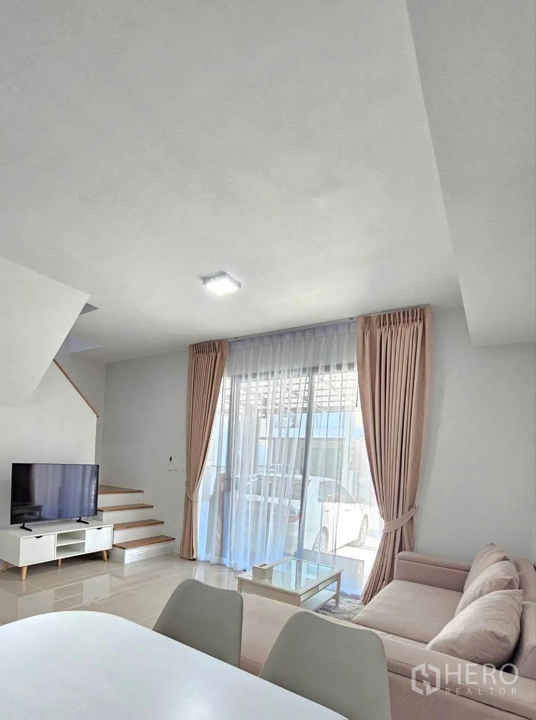 Townhouse for rent in Bang Phli, Samut Prakan - Living room with TV console, stairs and sliding door opening to the carport.