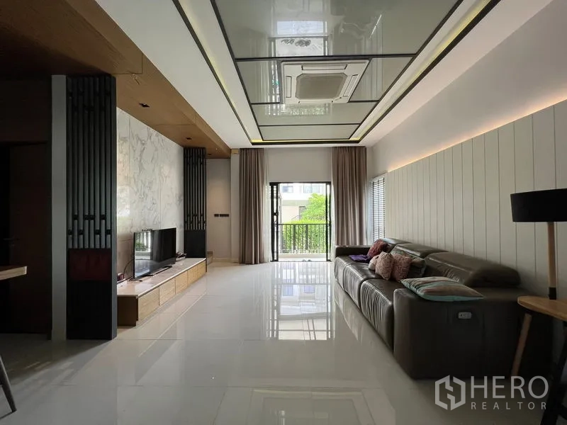 Townhouse for rent in Saphan Sung, Bangkok - Long lounge with TV wall, balcony doors, and coffered ceiling with ducted air-conditioning.