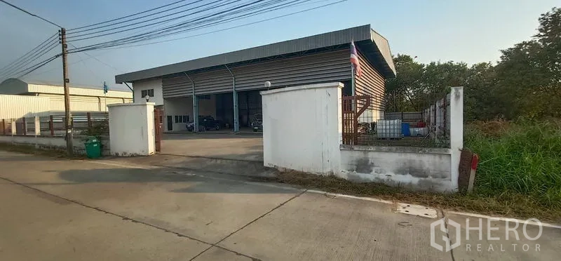 货栈 出租在Khlong Luang, Pathum Thani - 仓库正立面，低矮围墙与临路出入口。