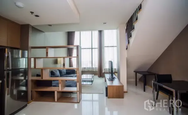 Condominium for rent or sale in Khlong Toei, Bangkok - Living area with floor-to-ceiling windows, shelving divider, and stairs to mezzanine.