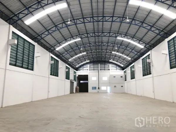 Factory for rent or sale in Bang Sao Thong, Samut Prakan - Spacious warehouse interior featuring a high arched steel roof, bright strip lighting, and concrete floor.