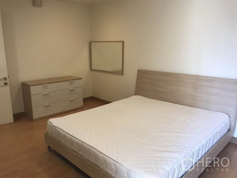 Condominium for rent in Khlong Toei, Bangkok - Bedroom with double bed, dresser and wall mirror in neutral tones.