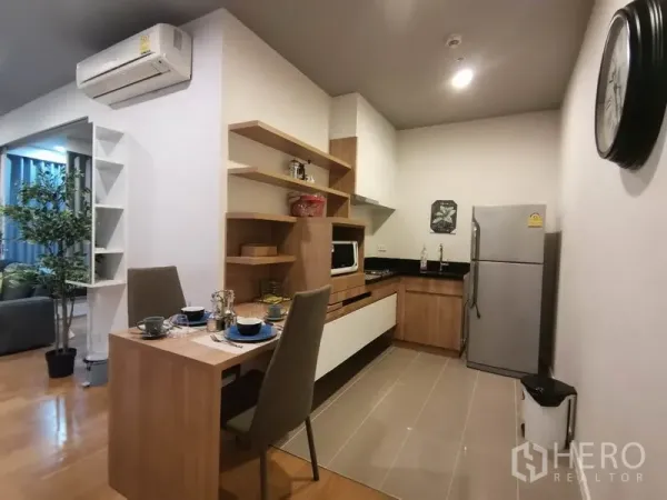 公寓 出租或出售在Watthana, Bangkok - 木质橱柜与开放层架的紧凑厨房，配双人餐桌和不锈钢冰箱。