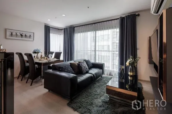 Condominium for rent in Khlong Toei, Bangkok - Cozy living room with sofa, glossy coffee table, dining set, and floor-to-ceiling balcony doors.