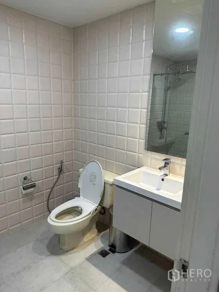 Condominium for sale in Bangkok - Modern bathroom with square tiled walls, vanity, mirror and toilet with bidet spray.