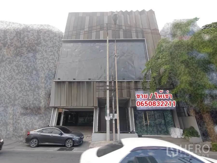 带办公室的家 出租或出售在Phra Khanong, Bangkok - 现代多层家庭办公楼外立面，金属板与玻璃门面，临街可停车，靠近BTS Bang Chak站。