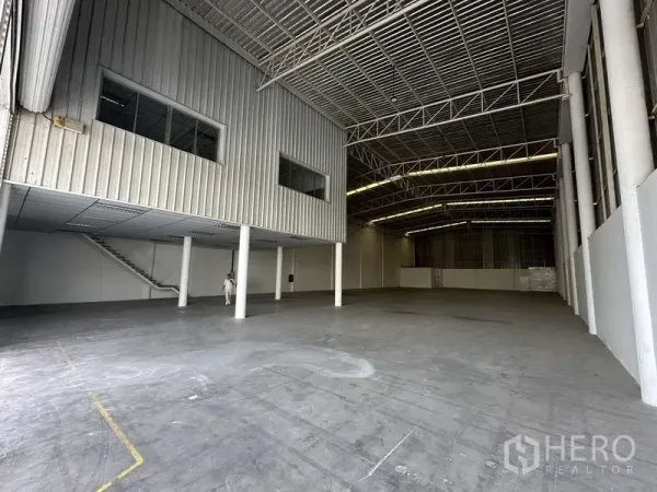 Factory for rent in Khlong Luang, Pathum Thani - Spacious warehouse interior with high ceiling, steel trusses, and a mezzanine office with stairs.