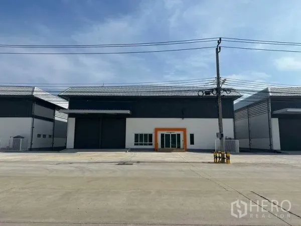 Factory for rent in Bang Sao Thong, Samut Prakan - Modern factory facade with large roller shutter doors, glass office entrance and a wide concrete driveway.