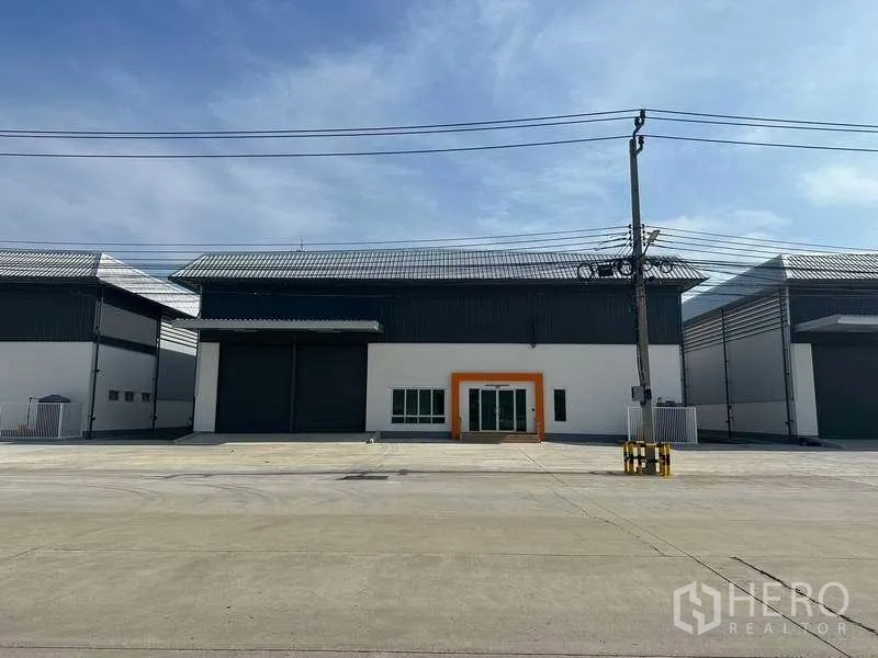 Factory for rent in Bang Sao Thong, Samut Prakan - Modern factory facade with large roller shutter doors, glass office entrance and a wide concrete driveway.