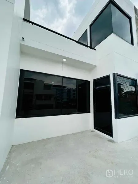 带办公室的家 出租或出售在Suan Luang, Bangkok - 白色两层家办外立面，大型黑色窗框与水泥庭院。
