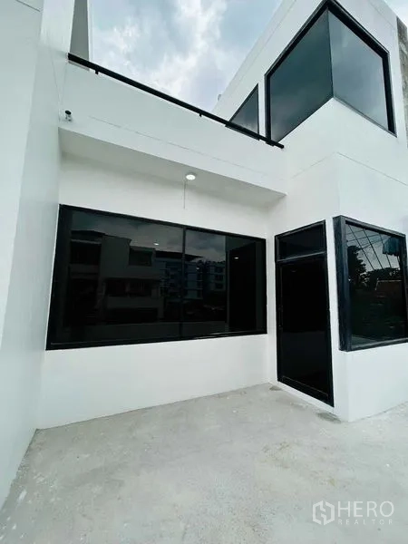 带办公室的家 出租或出售在Suan Luang, Bangkok - 白色两层家办外立面，大型黑色窗框与水泥庭院。