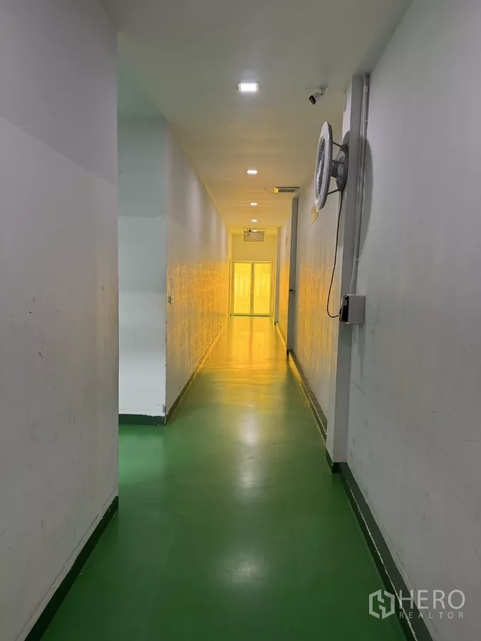 工厂 出售在Lam Luk Ka, Pathum Thani - 工业走道，绿色环氧地坪，墙挂风扇，尽头为黄色灯光区。