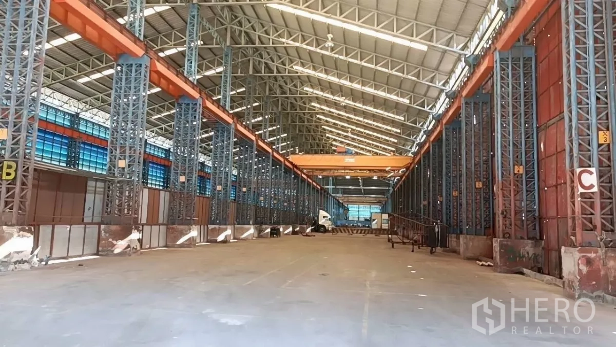Warehouse for rent in Mueang Samut Sakhon, Samut Sakhon - Long central aisle with twin overhead cranes, multiple loading bays, and truck access beneath a high roof.