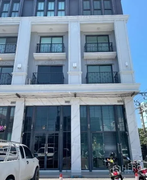 Home Office for rent or sale in Suan Luang, Bangkok - Contemporary 4.5-storey home office façade with tall glass shopfront and upper-floor balconies, with parking area in front.